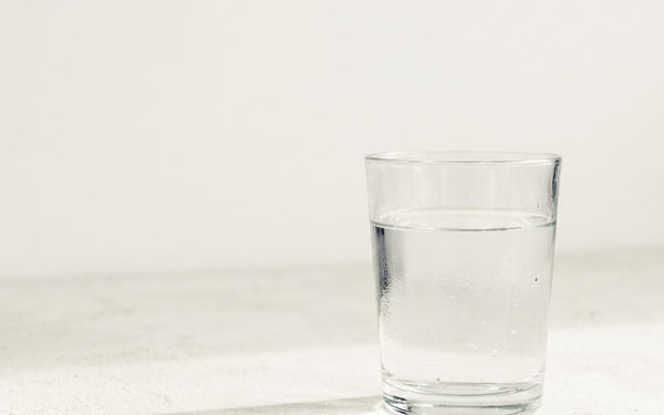 A single pint glass of clear water on a pale concrete surface in soft morning light, condensation on the glass, nothing else in frame
