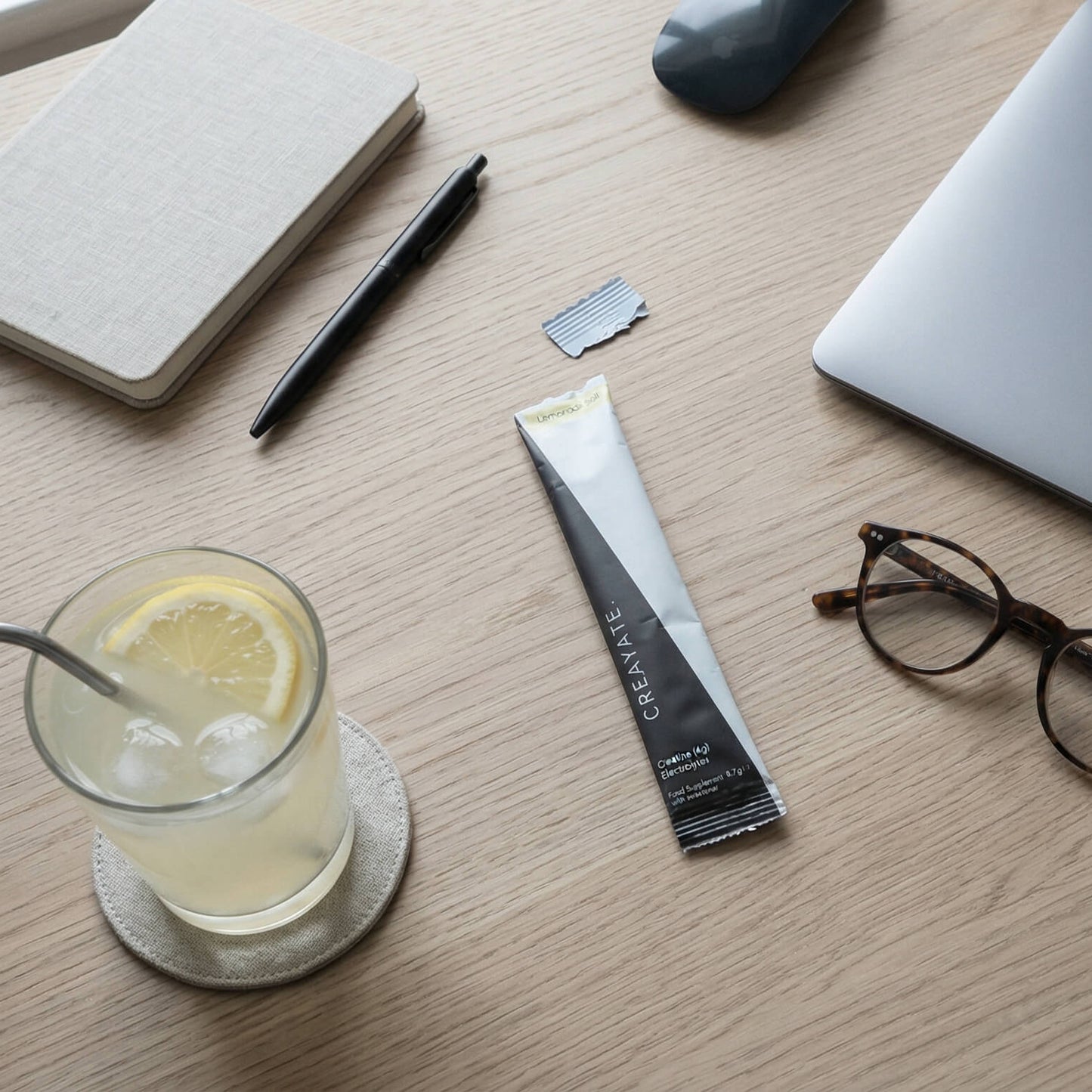 CREAYATE creatine electrolyte sachet on a desk with lemonade salt mixed drink, notebook, pen and laptop